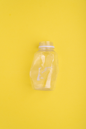 Crashed plastic bottle on yellow background. Plastic utilisation concept. Ecological problem, global environment.の写真素材