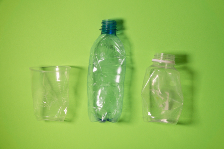 Crashed plastic bottles and a cup on bright green background. Plastic utilisation concept. Ecological problem, global environment.の写真素材