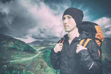 Active young man hiking in the mountain, side view on cloudy landscape background. Active lifestyle and tourism.の写真素材