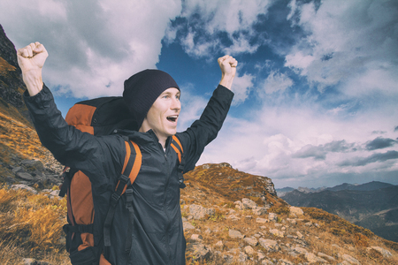 Young hiker shouting out on top with his hands raised, side view.の写真素材