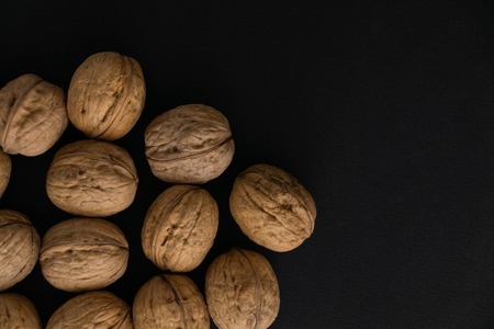 Walnuts in the shell on black surface, top view. Background of round walnuts. Healthy nuts and seeds composition.の写真素材