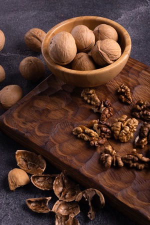 Walnuts in wooden bowl on wooden carved board. Healthy nuts and seeds composition.