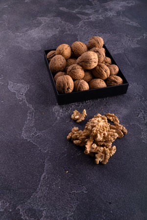 Whole and cracked walnuts on a square plate on blue textured surface, side view. Healthy nuts and seeds composition.の写真素材