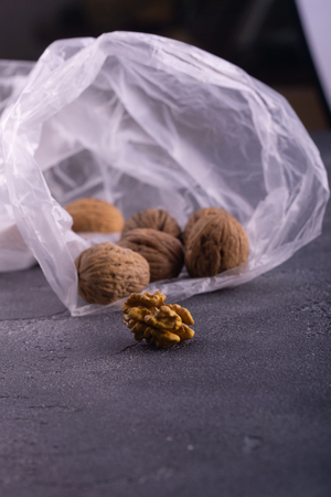 Whole and cracked walnuts in open plastic bag on blue textured surface, side view. Healthy nuts and seeds composition.の写真素材