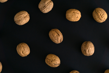 Walnuts in the shell on black surface, top view. Background of round walnuts. Healthy nuts and seeds composition.の写真素材