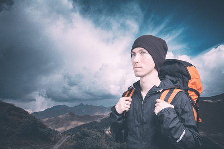 Active young man hiking in the mountain, side view on cloudy landscape background. Active lifestyle and tourism.の写真素材