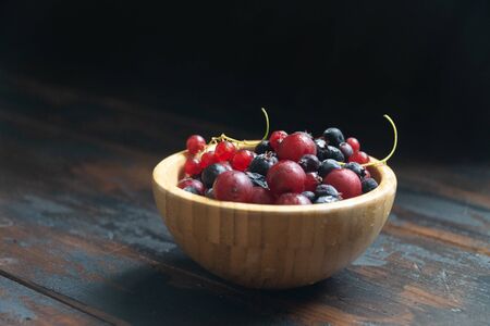 Ripe black and red currants in a wooden bowl on a wooden table. Organic food, berries, harvest season.の写真素材