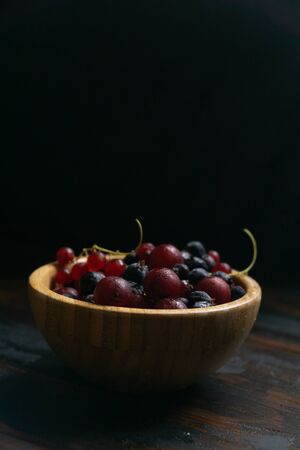 Ripe black and red currants in a wooden bowl on a wooden table. Organic food, berries, harvest season.の写真素材