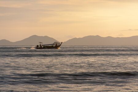 Traditional long boat sailing by the island in the evening, Thailand.