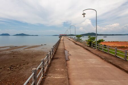 Long pier at Koh Phangan island, during low tide with clouds, boats, and mountains on the background.の写真素材
