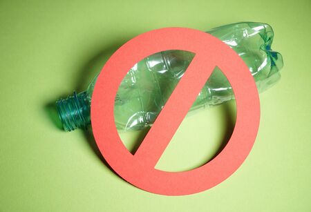 Squeezed empty blue plastic bottle in a stop sign on green background. Concept of stop plastic pollution, recycling plastic, plastic free.の写真素材