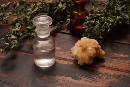 Two vials, dried leaves, and a crystal on rustic wooden table.の写真素材