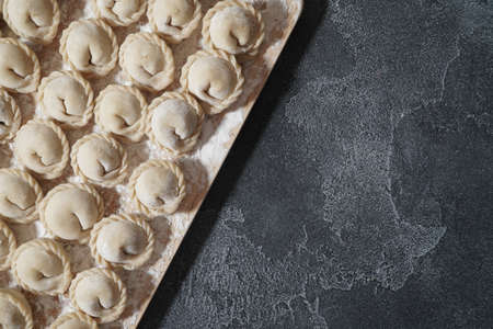 Meat or vegeterian dumplings, pelmeni on a wooden board on a dark grey table. Russian national food. Close up top view.の写真素材