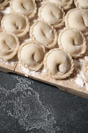 Meat or vegeterian dumplings, pelmeni on a wooden board on a dark grey table. Russian national food. Close up top view.の写真素材