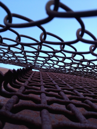 View into the blue through the webbed chain linked fence 