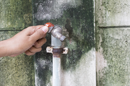 hand touch old rusty water tap by the wall prepare to open the tap. the wall look damp and cover with green algae.の写真素材