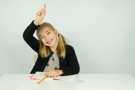 Cute girl is raising her hand in the classroom. She knows the answer the teacher askedの写真素材