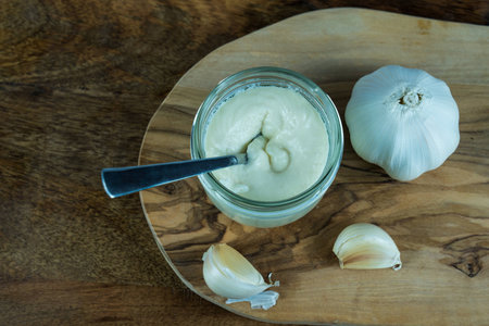 Garlic on a olive wooden plate. on the wooden plate is also a jar with home made aioliの写真素材