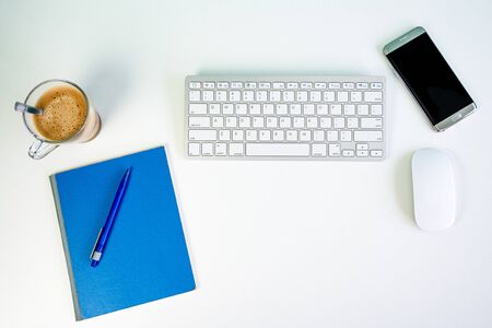 white office desk with wireless keyboard, mouse, smartphone, cup of coffee, pencil and a writing blockの写真素材