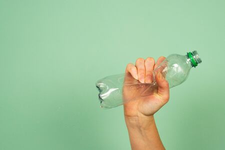 Woman's hand holding smashed empty plastic water bottle not used, concept or recycling