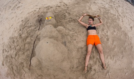 Smiling sandy snowman in red santa hat on the sea beach. Holiday concept can be used for New Year and Christmas Cardsの写真素材