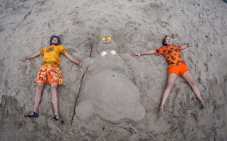 Smiling sandy snowman in red santa hat on the sea beach. Holiday concept can be used for New Year and Christmas Cardsの写真素材