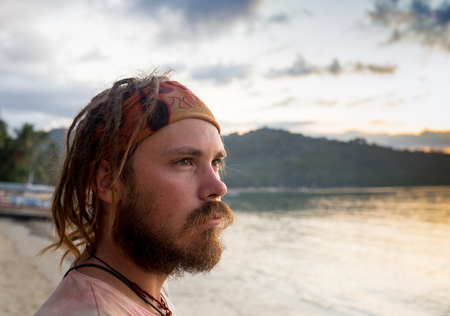 Young man standing on coastline and enjoying beautiful sunset over the sea. Image with sunlight effectの写真素材