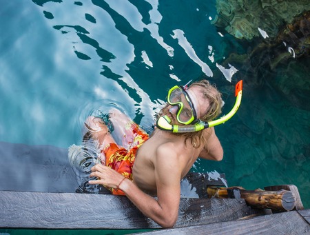 Young man snorkeling in clear shallow tropical sea over coral reefsの写真素材