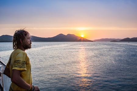 Young man standing on coastline and enjoying beautiful sunset over the sea. Image with sunlight...