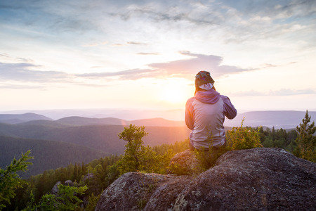 Young woman sitting on a rock with backpack and looking to the horizon