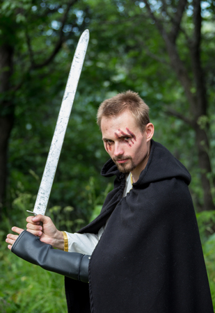 Portrait of a beautiful young warrior holding sword in golden lightの写真素材
