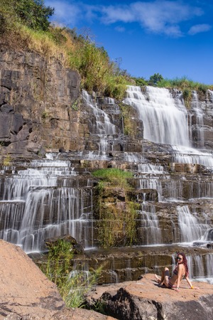 Bikini girl sitting next to idyllic tropical waterfall in Thailandの写真素材