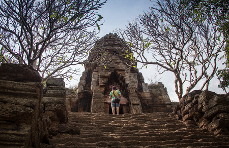 Young female tourist with smartphone taking picture of the gopura under blue sky near the entrance to ancient Preah Khan temple in Angkor. Siem Reap, Cambodia.の写真素材