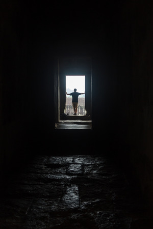 Male silhouette in empty interior looking in window, lit by dramatic sunlightの写真素材