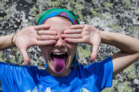 A toddler girl with a colorful, ice cream colored tongue, sticks it out at the camera. Her face is messy with icing.の写真素材