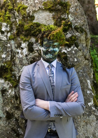Office worker in a business suit, outdoors with a make-up on his face and green moss on his head. Man merges with nature.の写真素材