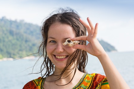 A girl is holding a seashell on the background of a sea landscapeの写真素材