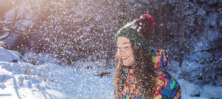Happy winter fun woman throwing snow banner. Panorama crop of outdoor lifestyle girl playing in snow outside laughing in yellow coat, hat, gloves and scarf.の写真素材