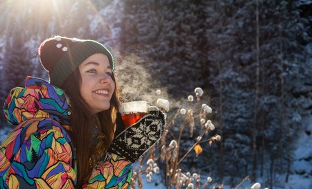 Girl enjoys the snow falls. Young woman in a knitted shape is drinking tea in the forest during a snowfall. Toned photoの写真素材