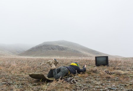 Girl on the nature lying on the ground and watching an old TV