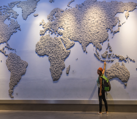 Confident casual woman standing alone in front of the world map hole as a window shaped in a...
