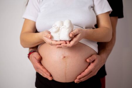 Cropped image of beautiful pregnant woman and her handsome husband hugging the tummy.