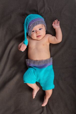 Beautiful baby girl in the studio on a dark gray background in bare pants and a winter hatの写真素材
