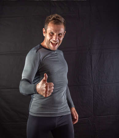 Handsome shirtless fitness man in gray shorts, smiling and posing against dark black background. Mild retouch, studio lighting.の写真素材