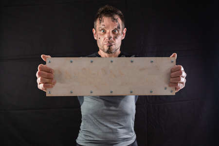 A sporty man holding an empty wooden sign with screws on a black background. Concept for inserting any wordの写真素材