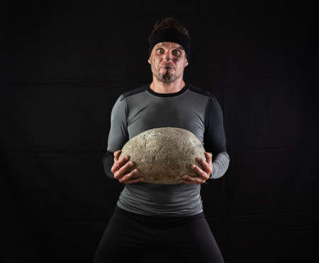 Sporty man holding a large heavy stone in his hands on a black backgroundの写真素材