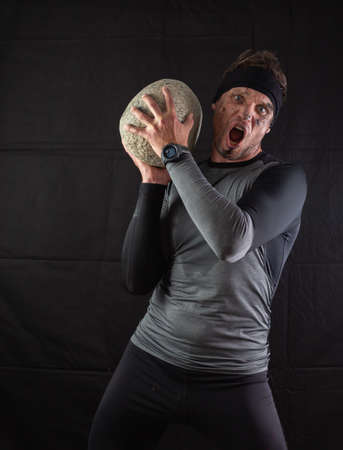 Sporty man holding a large heavy stone in his hands on a black backgroundの写真素材