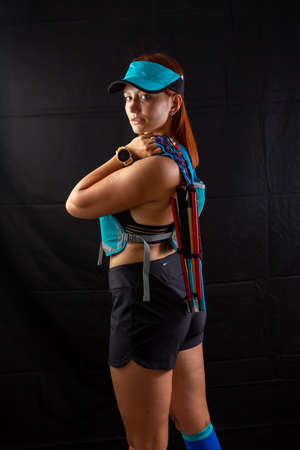 Beautiful girl marathon runner in blue jogging equipment and trekking poles in the studio on a black backgroundの写真素材