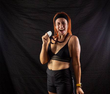 Beautiful redhead girl in sportswear with a silver medal in the studio on a black backgroundの写真素材