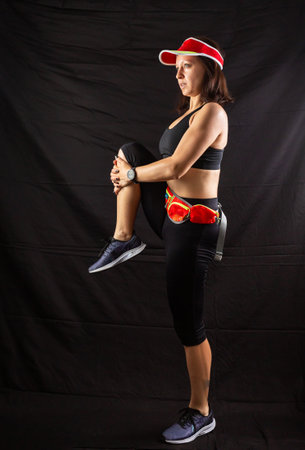 Beautiful girl in a jogging red uniform warming up before training in the studio on a black backgroundの写真素材